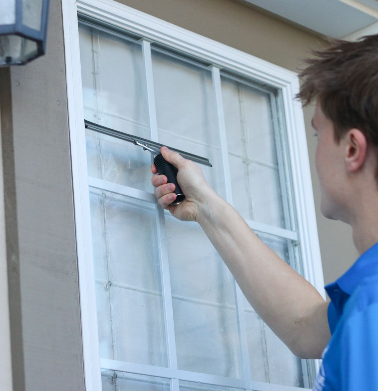 A Value Window Washing student cleaner squeegeeing an exterior window by hand